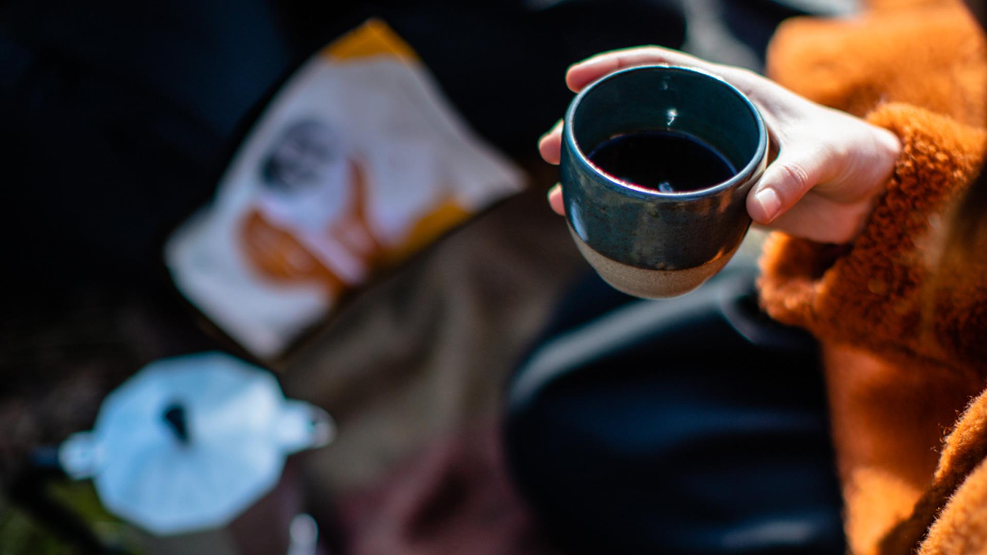 Hand holding mug with Sunny Joe coffee in background